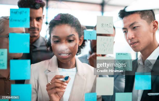 vielfältiges team, das an einer transparenten tafel mit haftnotizen in einer modernen büroumgebung zusammenarbeitet - geschäftsprozess stock-fotos und bilder