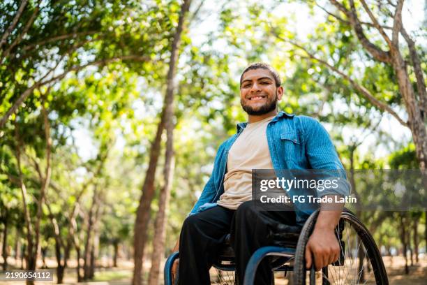 portrait of young wheelchair man on public park - rolstoel stockfoto's en -beelden