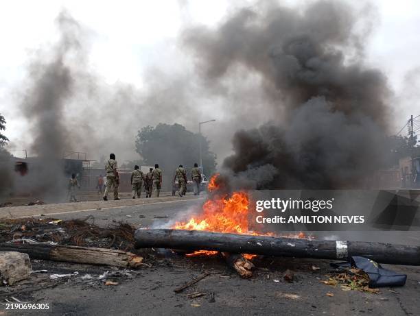 Pedestrians walk past a burning barricade in Maputo on December 24, 2024. The capital of Mozambique was deserted on Tuesday, its main arteries...