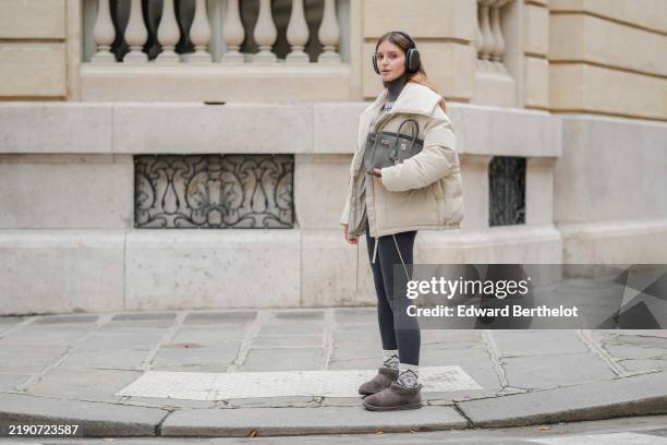 Diane Batoukina wears black headphones Airpods Max from Apple, a grey and white sweater, grey legging, a cream Varley bomber jacket, a grey leather...