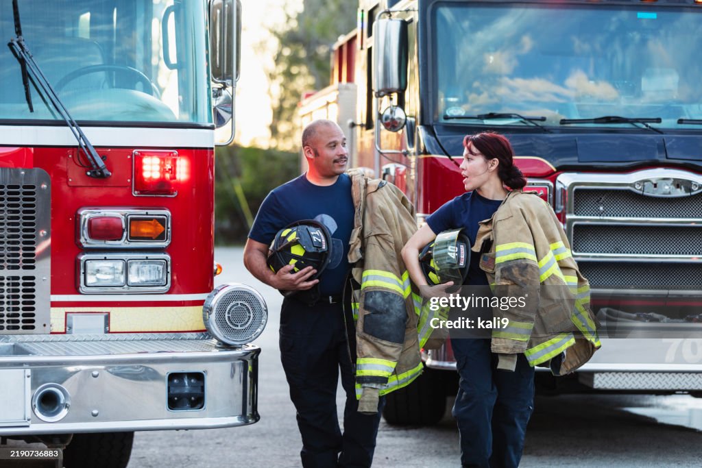 Two multiracial firefighters carrying protective gear