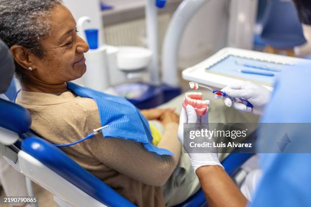 patient observing dental hygiene demonstration with toothbrush by professional - dentures stock pictures, royalty-free photos & images