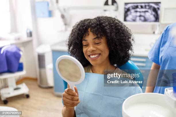 patient admiring her smile in a hand mirror after a dental care session - vulling tandartsapparatuur stockfoto's en -beelden