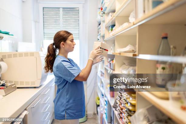 young woman dental assistant reviewing medicine in the office's pharmacy room - material médico fotografías e imágenes de stock