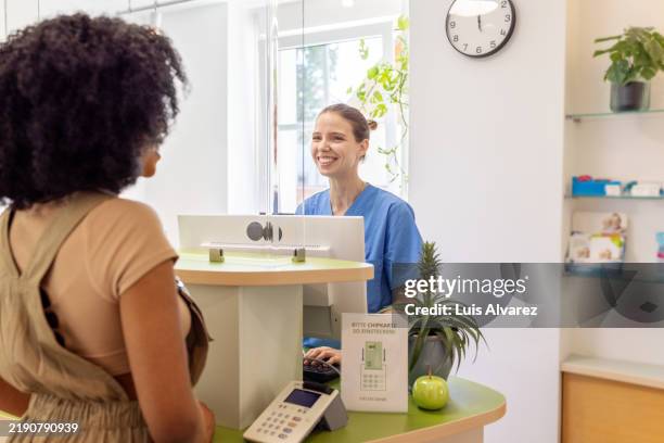 smiling dental receptionist assisting patient at reception desk - travel check in stock pictures, royalty-free photos & images