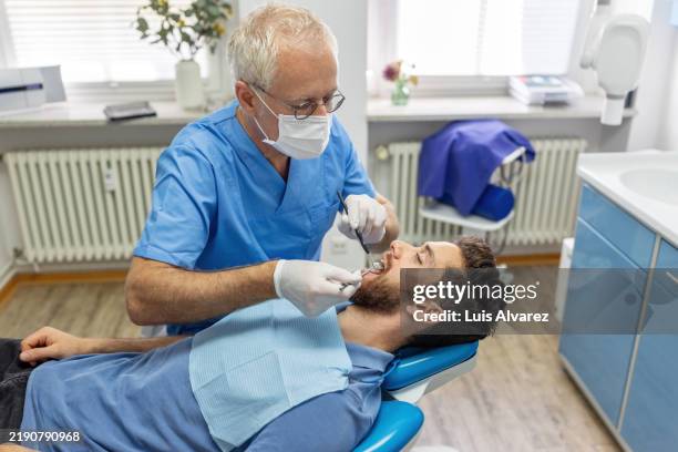 dentist and assistant providing dental care for patient - zahnarztstuhl stock-fotos und bilder