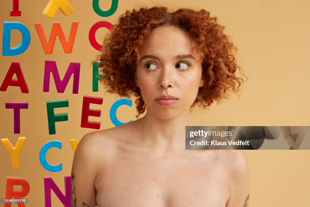 Thoughtful red haired non-binary person looking at alphabet