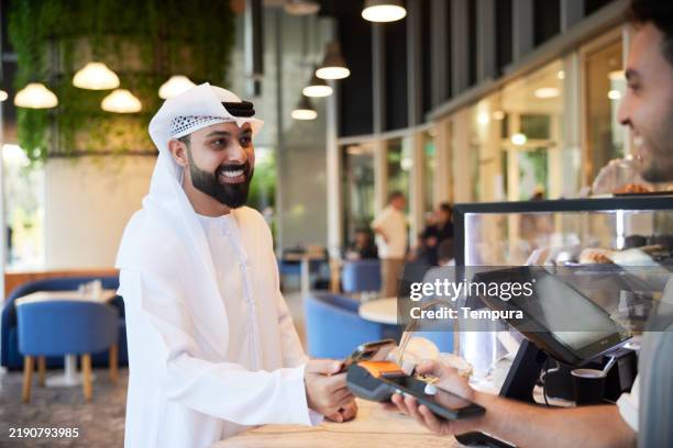 the coffee shop waiter is all set to charge a client with the pos system after serving the order. - emirati culture stock pictures, royalty-free photos & images