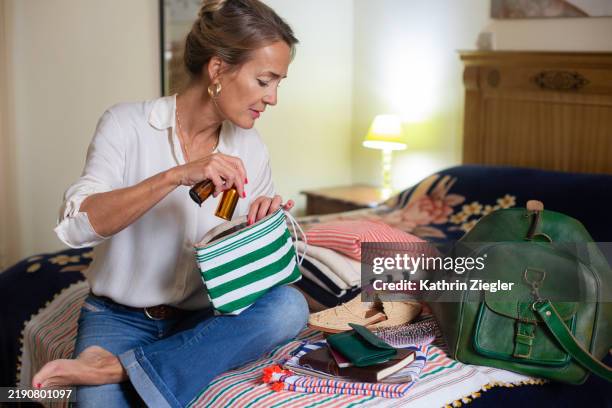 woman sitting on bed, packing for a trip - imballare foto e immagini stock