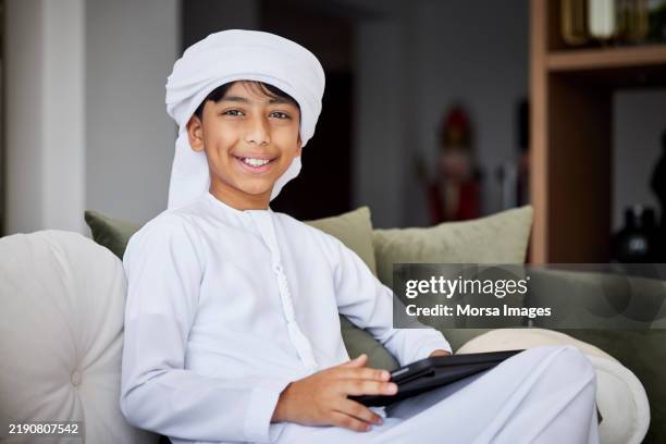 smiling middle eastern boy sitting on sofa - arabic boy stock pictures, royalty-free photos & images