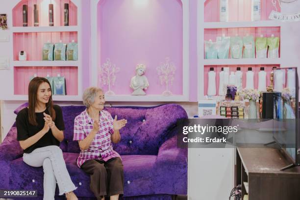 asian granddaughter and her grandmother are watching tv shows at the salon. - hair salon images free stock pictures, royalty-free photos & images