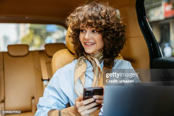 junge frau, die das telefon benutzt und arbeitet an einem laptop, während sie auf dem rücksitz eines taxis in shanghai in china fährt - mobility as a service stock-fotos und bilder