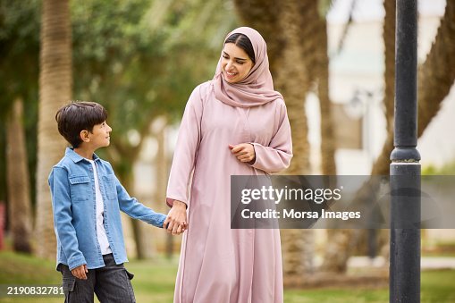 Saudi woman holding hand of son and walking at park Saudi woman holding hand of son and walking at park