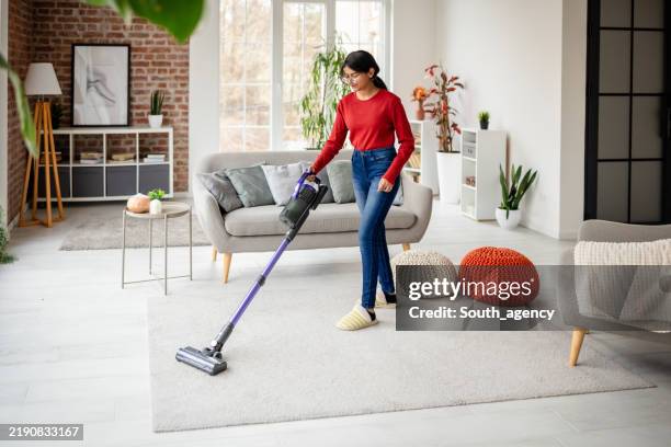 donna che passa l'aspirapolvere nel soggiorno moderno con accenti decorativi - aspirapolvere foto e immagini stock