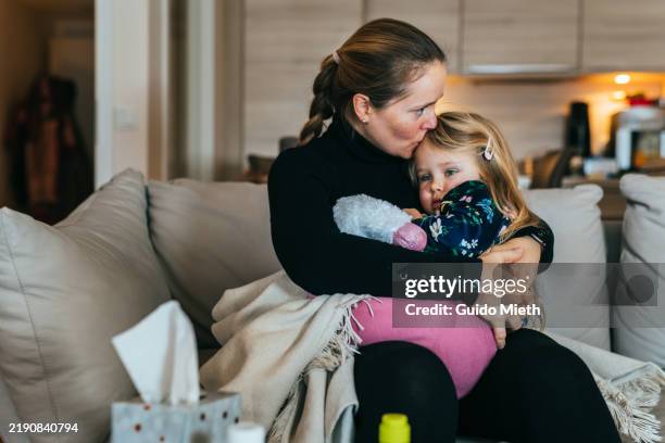 mother embracing her little sick daughter on sofa at home. - yngre skolåldern bildbanksfoton och bilder