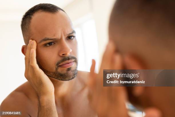young man touching his face while looking in mirror - perfect man stock pictures, royalty-free photos & images