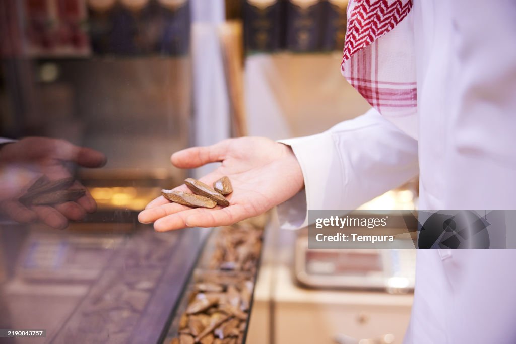 A close-up view shows a hand delicately holding wooden oud incense