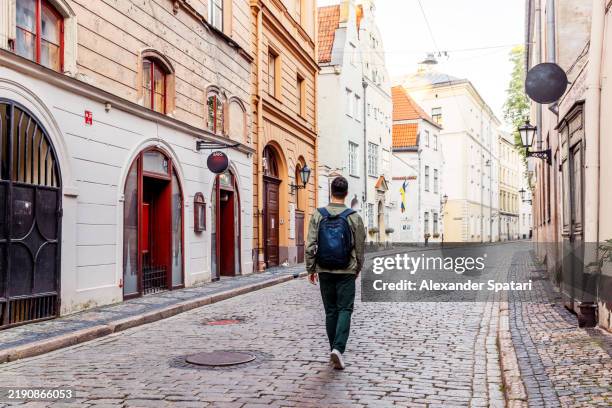 man with backpack exploring charming streets of riga old town, latvia - riga stock pictures, royalty-free photos & images