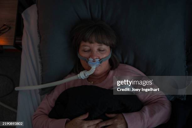 top-down-aufnahme einer älteren erwachsenen frau, die ein cpap-gerät (kontinuierlicher positiver atemwegsdruck) trägt, nachdem bei ihr schlafapnoe diagnostiziert wurde - schlafapnoe stock-fotos und bilder