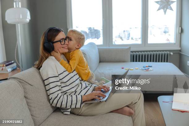 mother multitasking with remote work and parenthood on a cozy sofa - working parents stock pictures, royalty-free photos & images