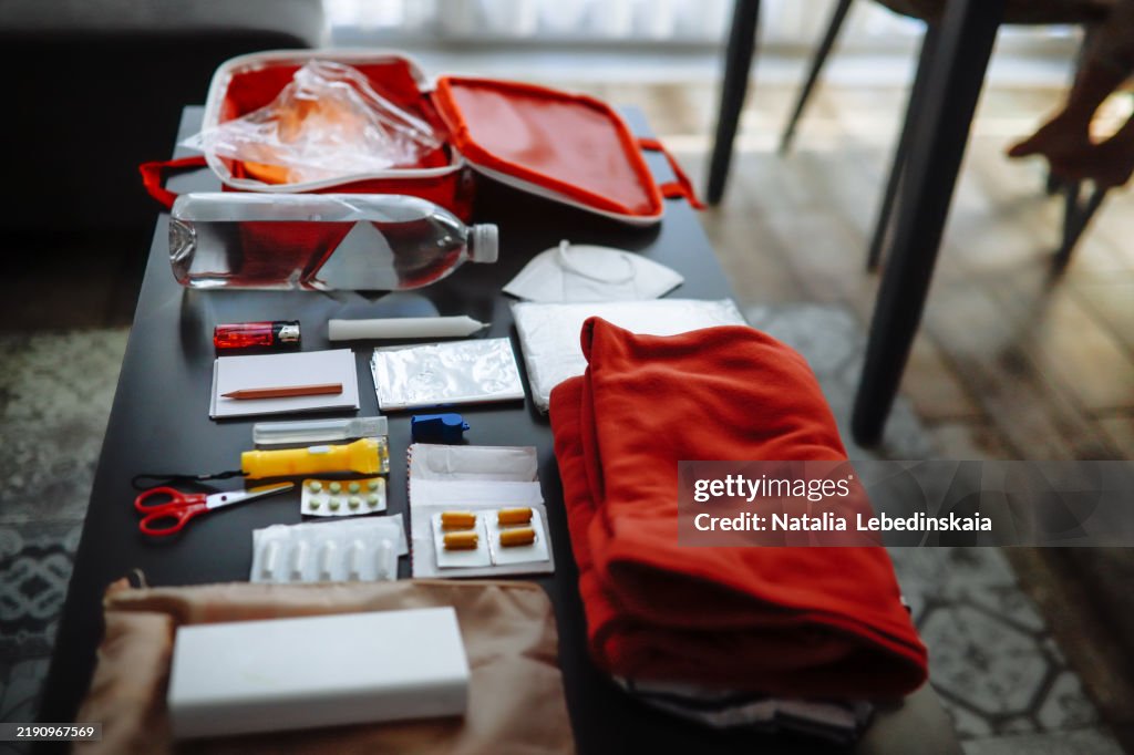 Doomsday prepping essentials: water, protective gear, whistle, raincoat, and tools for emergencies, shown in a cozy home flat lay.