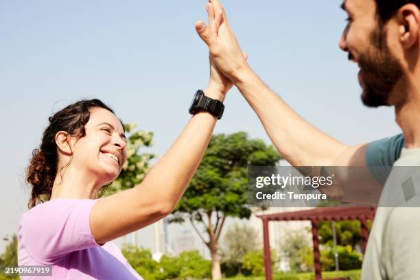 after completing their run in the park, the couple greets each other with a joyful high five, celebrating their achievement together. - north african culture stock pictures, royalty-free photos & images