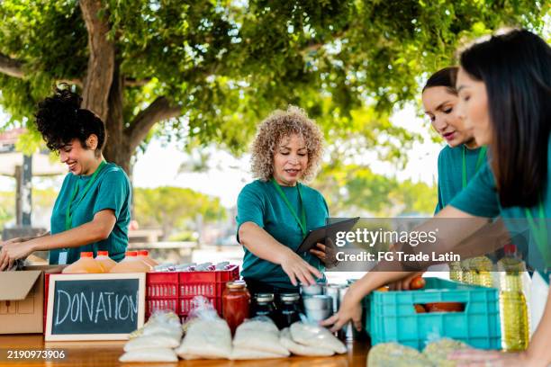mature woman talking and organizing donation boxes with volunteers outdoors - banco alimentar imagens e fotografias de stock
