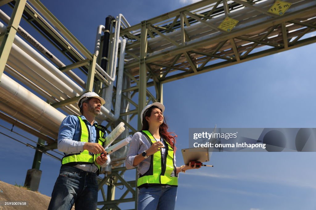 Female and male piping system engineers working at the pipeline construction in the refinery or chemical plant at an industrial estate