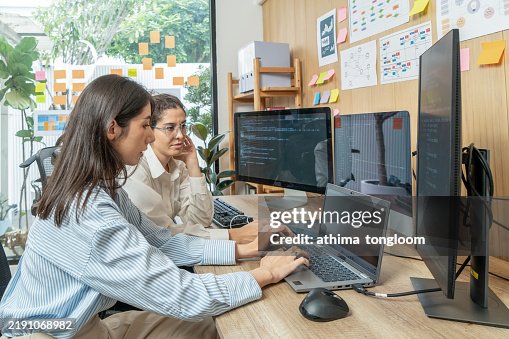Female Junior Software Engineer Writes Code on Desktop Computer With Two Monitors and Laptop Aside In Stylish Office. Female Junior Software Engineer Writes Code on Desktop Computer With Two Monitors and Laptop Aside In Stylish Office.