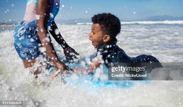 excited boy surfing with mother at beach - boogie board stock pictures, royalty-free photos & images