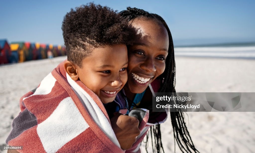 Smiling mother and son wrapped together in a towel on beach