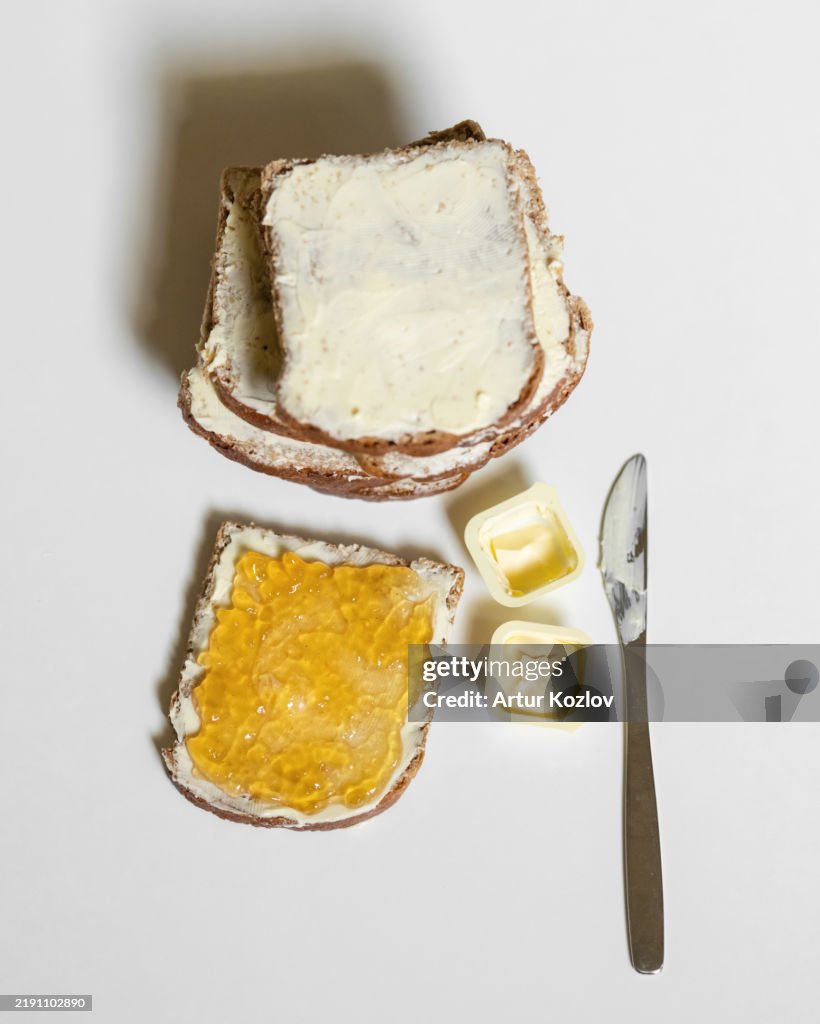 Bread slices, toast with butter, cream cheese and jam, jelly, marmalade. Sweet sandwich, knife, butter on white table. Sliced dark bread bricks with spread. Breakfast, snack, lunch. Top view.