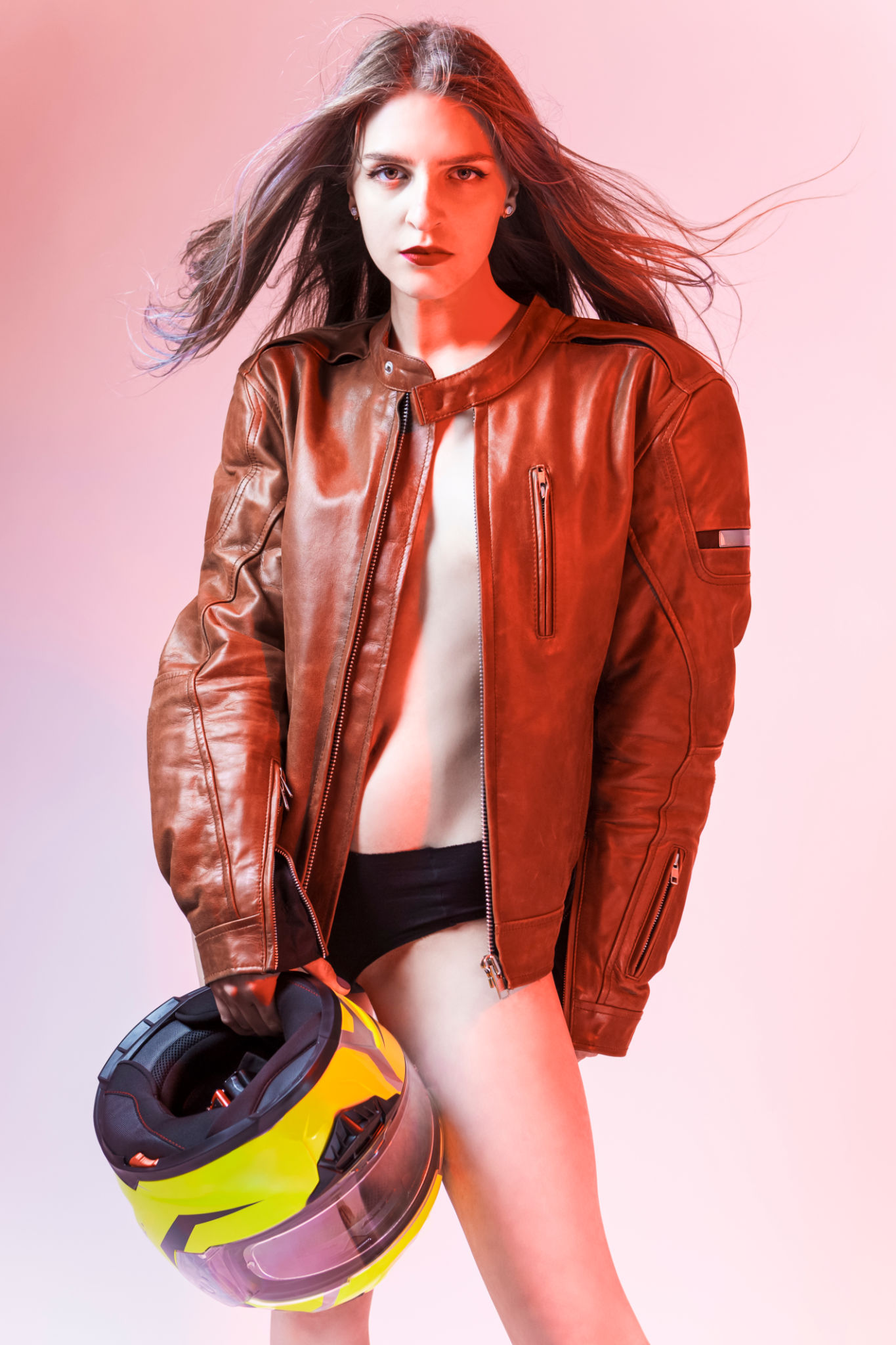 Natural Portrait of Sexy Caucasian Female Motorcyclist Posing In Leather Protective Jacket And Helmet Over Yellow Background. Natural Portrait of Sexy Caucasian Female Motorcyclist Posing In Leather Protective Jacket And Helmet Over Yellow Background.