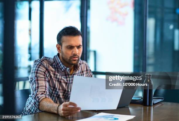 mid adult indian businessman looking at document with serious expression - paperwork stock pictures, royalty-free photos & images
