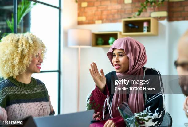 woman wearing pink hijab gesturing and explaining to colleague in meeting - religious dress stock pictures, royalty-free photos & images