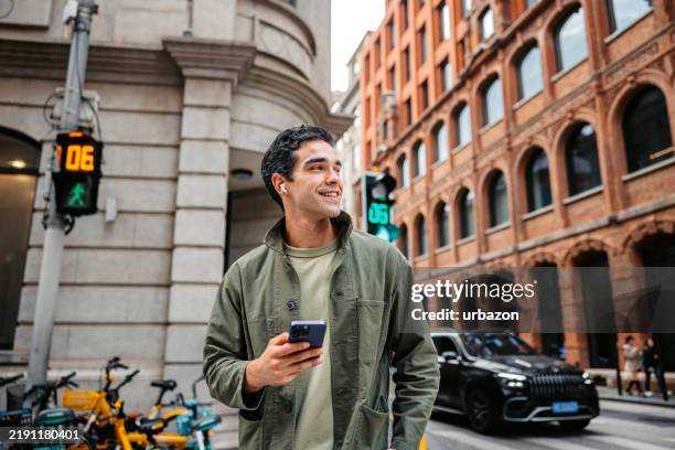 jeune homme utilisant son téléphone tout en écoutant de la musique dans la rue à shanghai en chine - jeunes hommes photos et images de collection