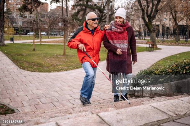 young female adult spending time with blind old person outdoors on winter day and walking together - cegueira imagens e fotografias de stock