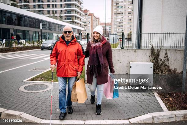 young female adult spending time with blind old person outdoors on winter day shopping together - blind persons cane stock pictures, royalty-free photos & images