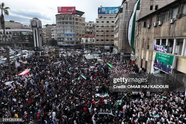 This aerial view shows people celebrating the ouster of Syria's president Bashar al-Assad, around the New Clock Tower in the centre of Homs on...