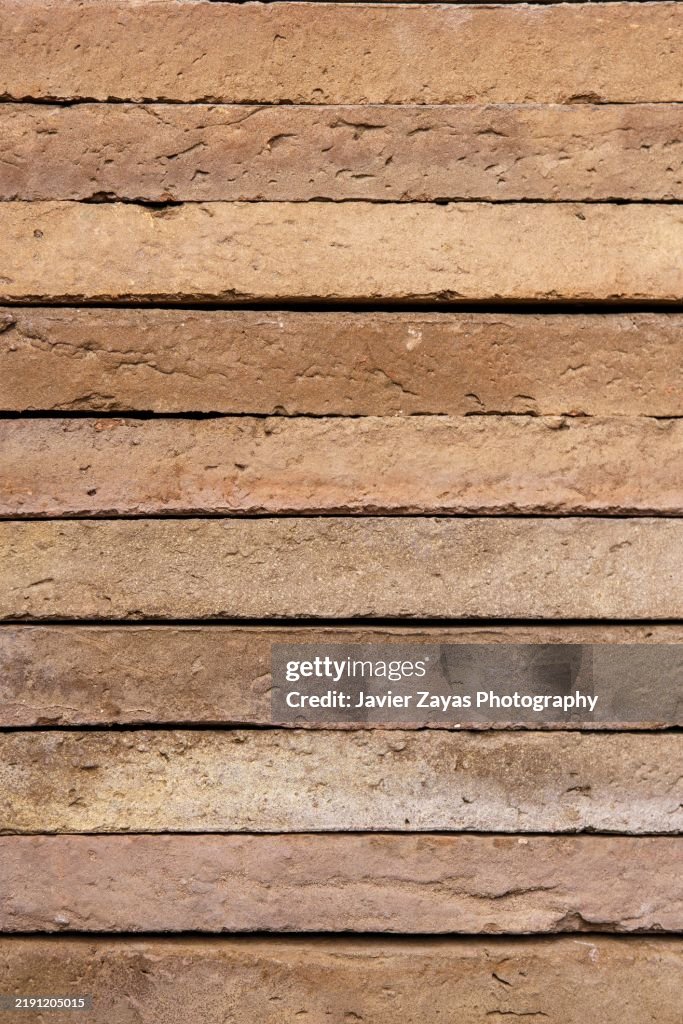 Mud bricks interlocking, displaying raw earthen texture, highlighting rustic construction materials with warm, natural coloring
