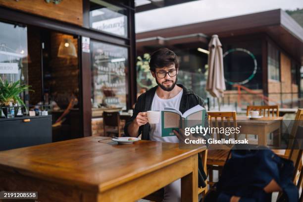 young intellectual man reading a book at an outdoor café - slow living stock pictures, royalty-free photos & images