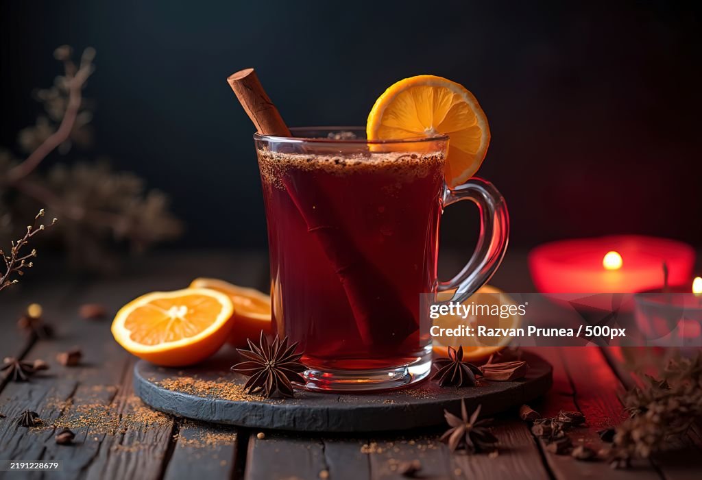 A glass of mulled wine with cinnamon sticks,Orange slices,And other spices on a wooden table with a dark background