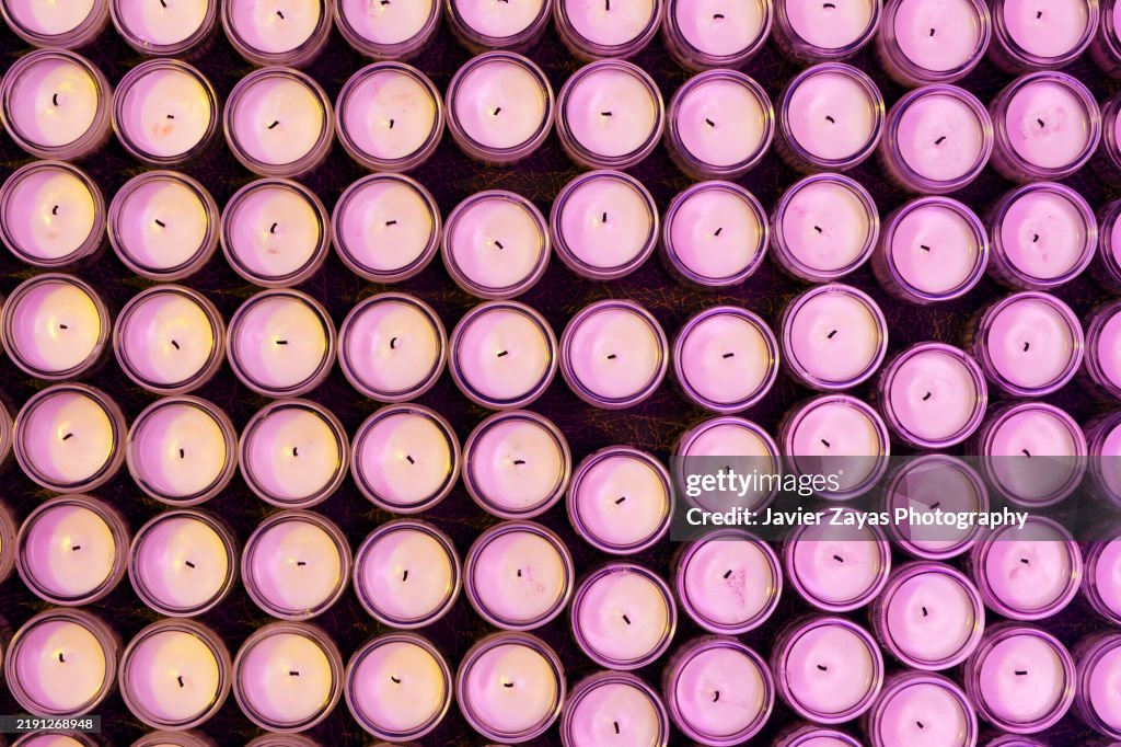 White candles gridded neatly, soft pink illumination casting delicate shadows across minimalist arrangement