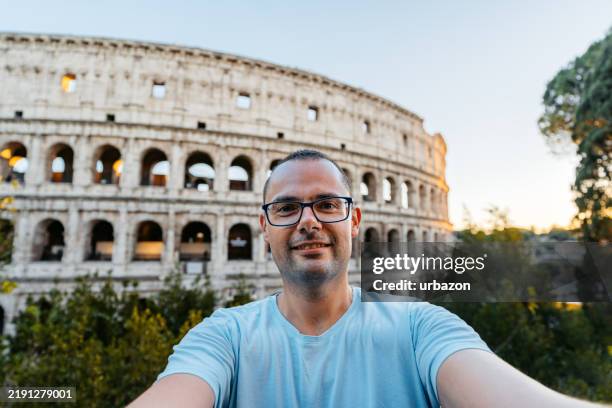mid-adult man taking selfies in front of the colosseum in rome in italy - roman amphitheater stock pictures, royalty-free photos & images