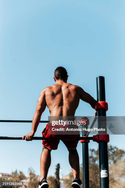 rear view of an athlete sitting on top of some calisthenics bars in a park. - macho photos et images de collection