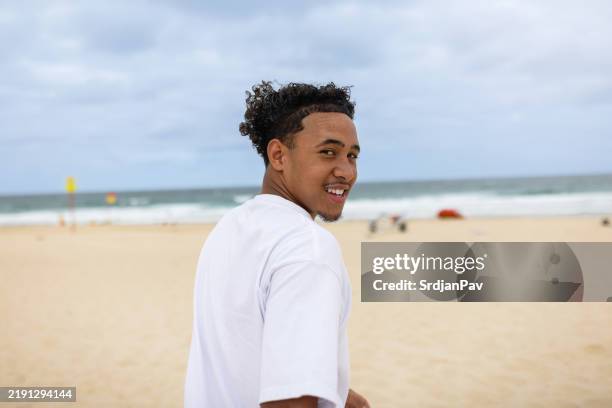un adolescent souriant des îles du pacifique sur la plage - regarder par dessus son épaule photos et images de collection