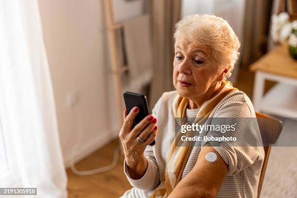 senior woman checking sugar or glucose level by tapping mobile phone to sensor at home - concept of technology, diabetes and health care - wearable computer stock pictures, royalty-free photos & images