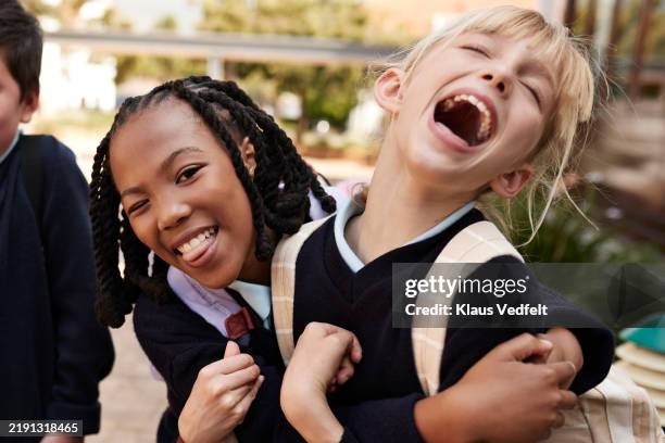 playful schoolgirl enjoying while embracing friend - school uniform stock pictures, royalty-free photos & images