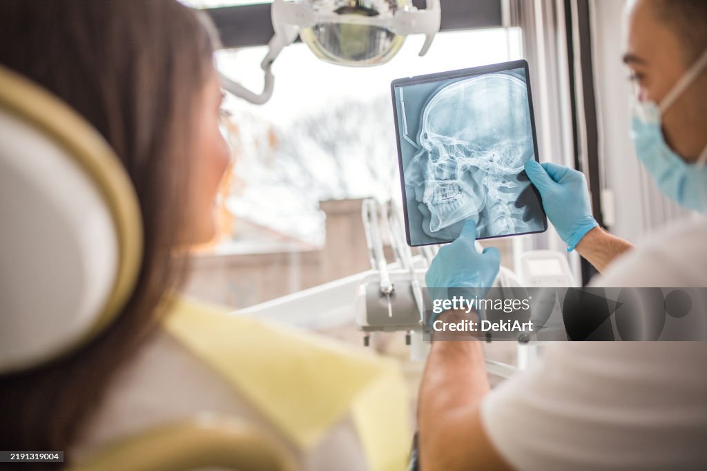 Ein Zahnarzt zeigt einer Patientin in der Zahnarztpraxis ein Röntgenbild des Ober- und Unterkiefers