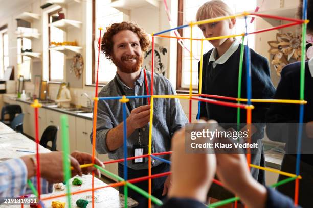 smiling teacher assisting students assembling straws - blue shirt stock pictures, royalty-free photos & images